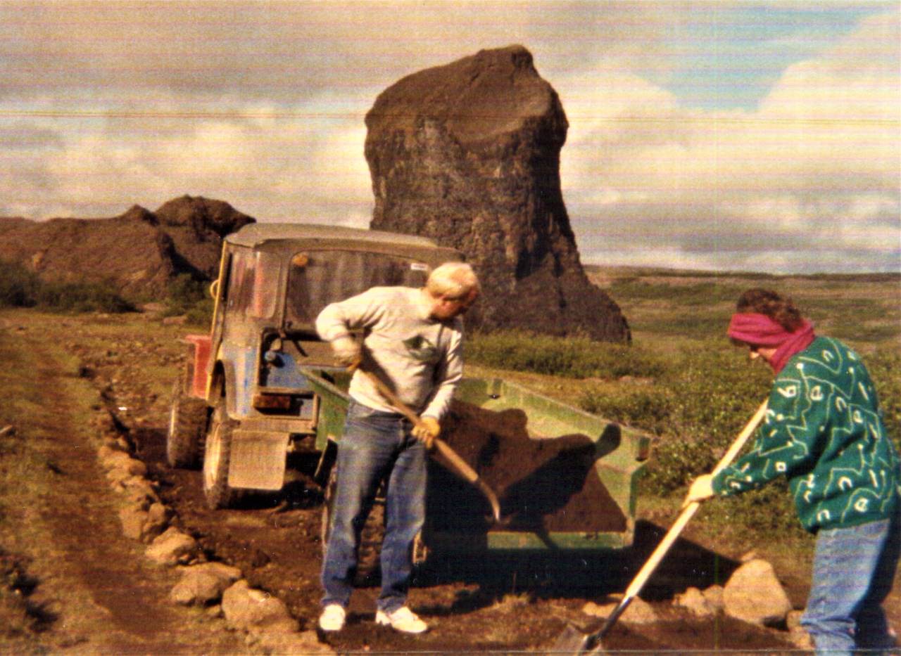 Kona og karl með skoflur að moka sand úr kerru á veg. Sjálfboðaliðasamtök um náttúruvernd leggja göngustíg við Hljóðakletta við Jökulsárgljúfur árið 1986.