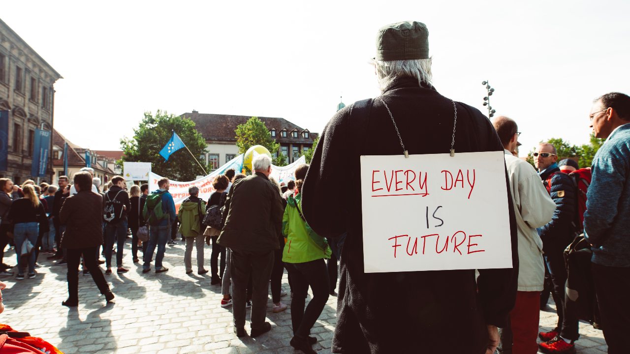 Sign on back of a man. Sign says "everyday is future" Hafðu áhrif.